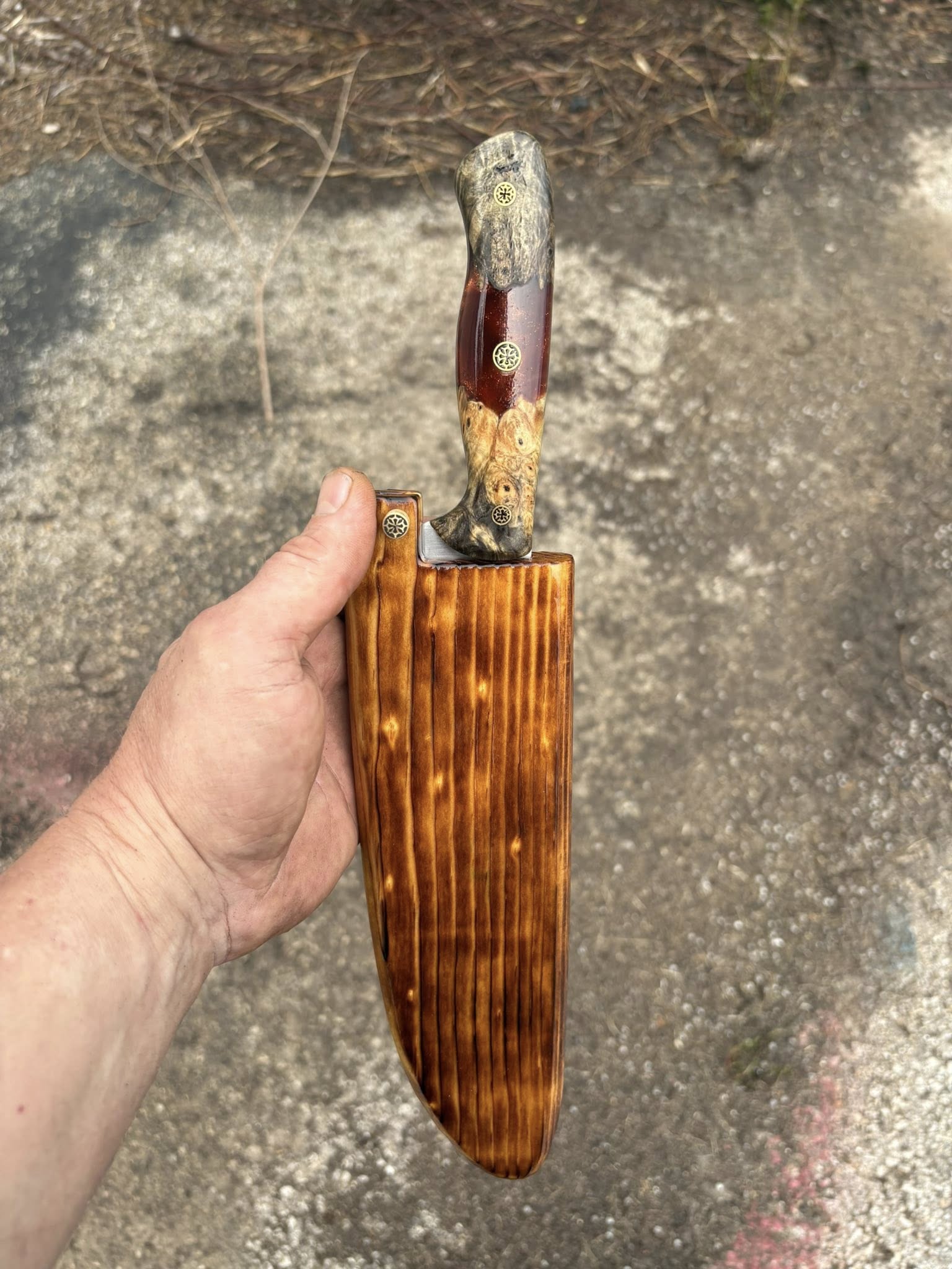Custom chef knife with multicolored handle resting in a charred-wood sheath, held in hand