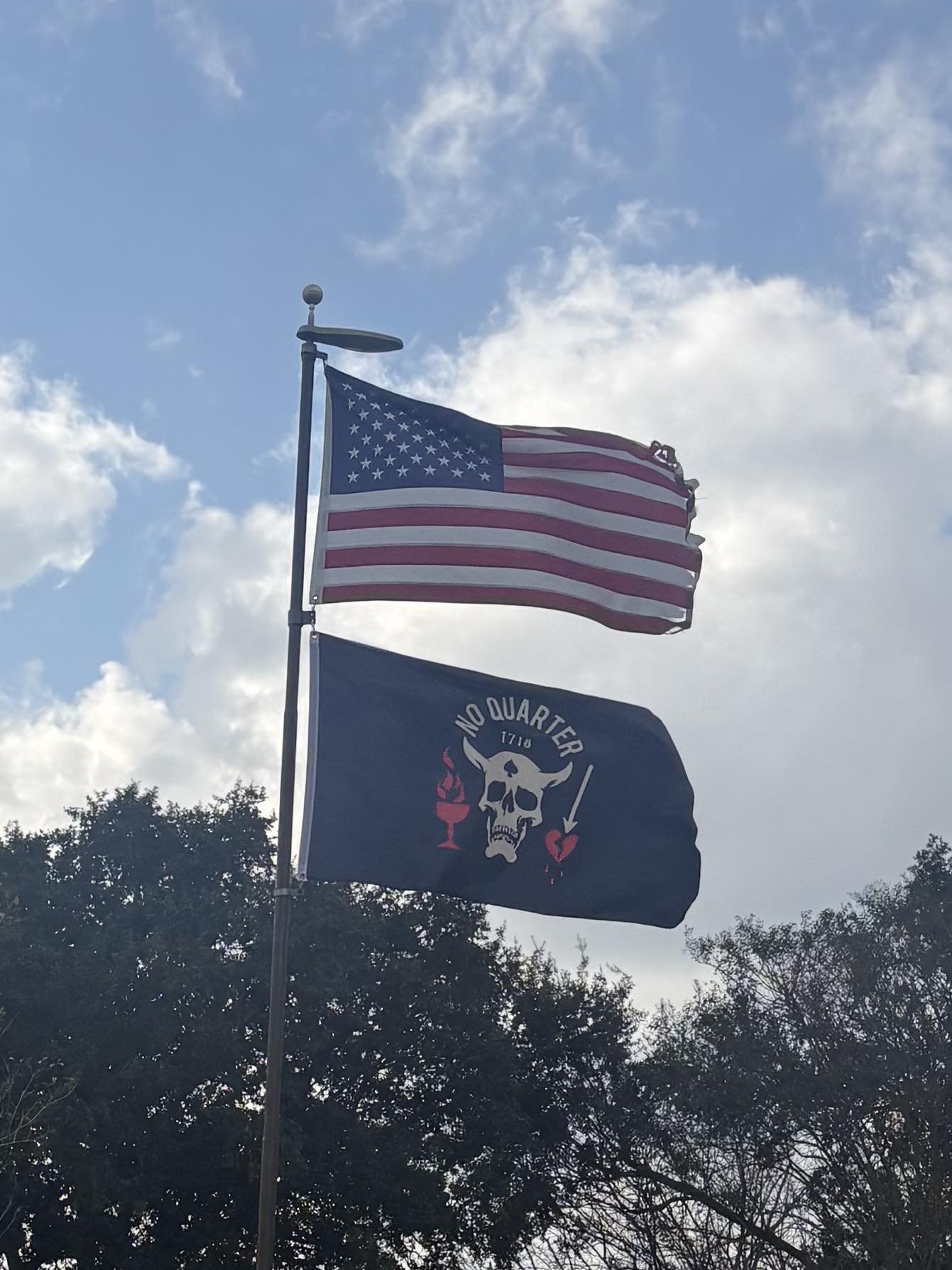 The No Quarter Knives flag flying outdoors below an American flag against a cloudy sky