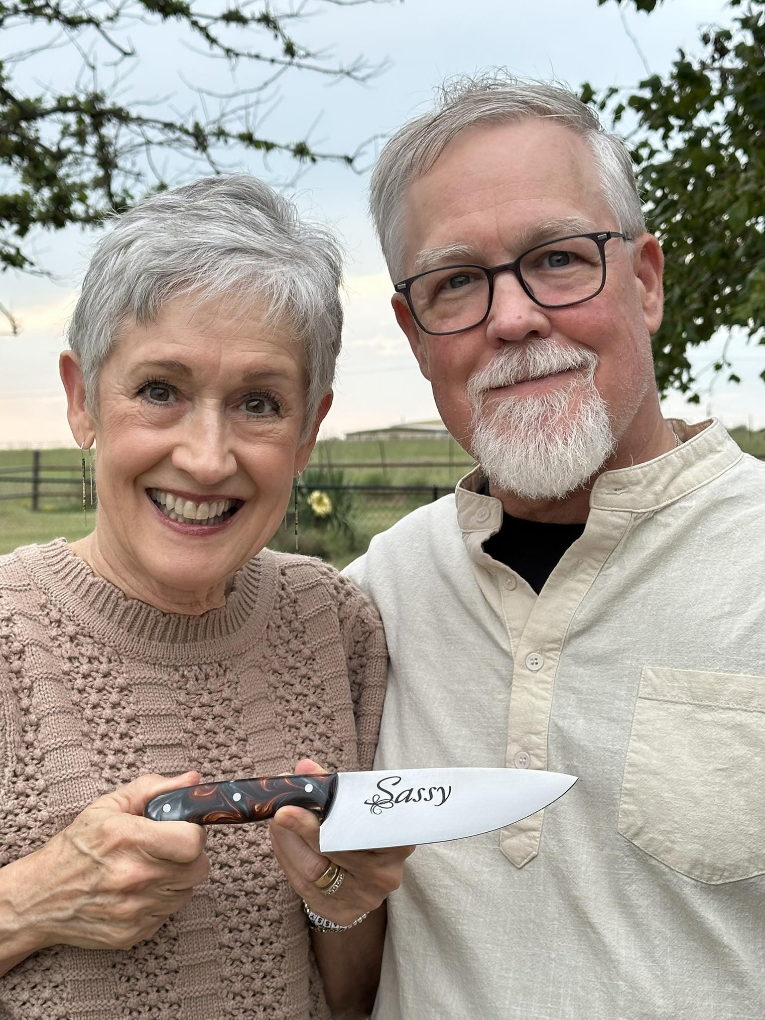 A couple smiling outdoors holding a custom chef knife etched with the name Sassy