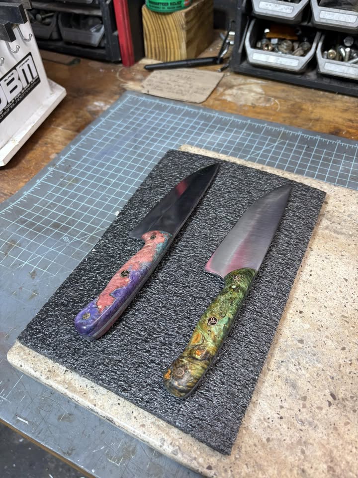 Two custom knives resting on a workshop bench